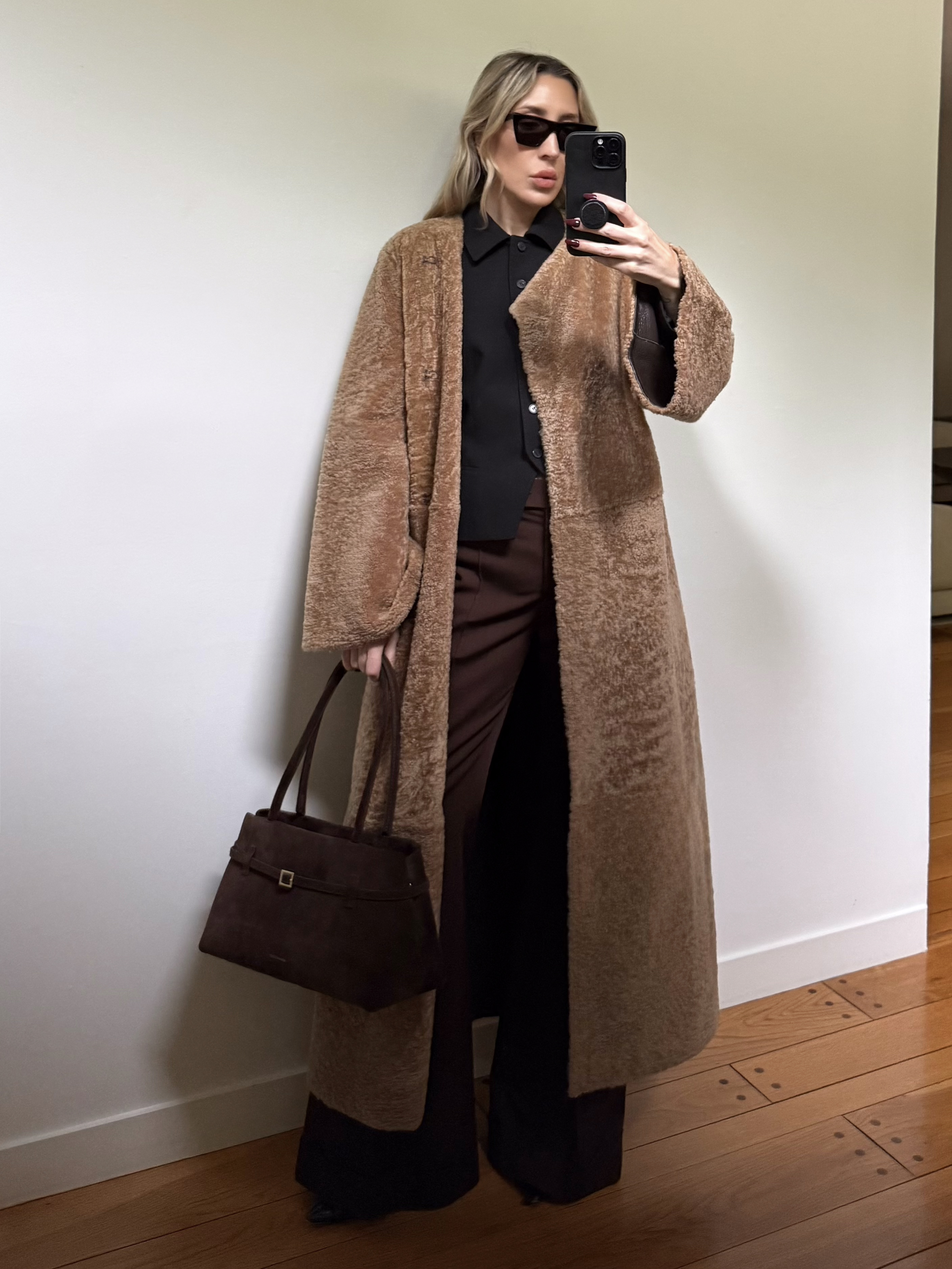 Angela Fink wearing a shearling coat, a button-down, pants, and a brown bag