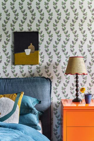 wallpapered bedroom with bright orange chest of drawers