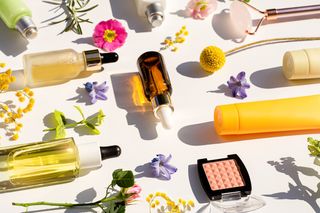 White background with multiple bottles of skincare products and flowers scattered around