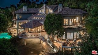 A large mansion estate at dusk with a pool, a balcony, and lights glowing through the windows