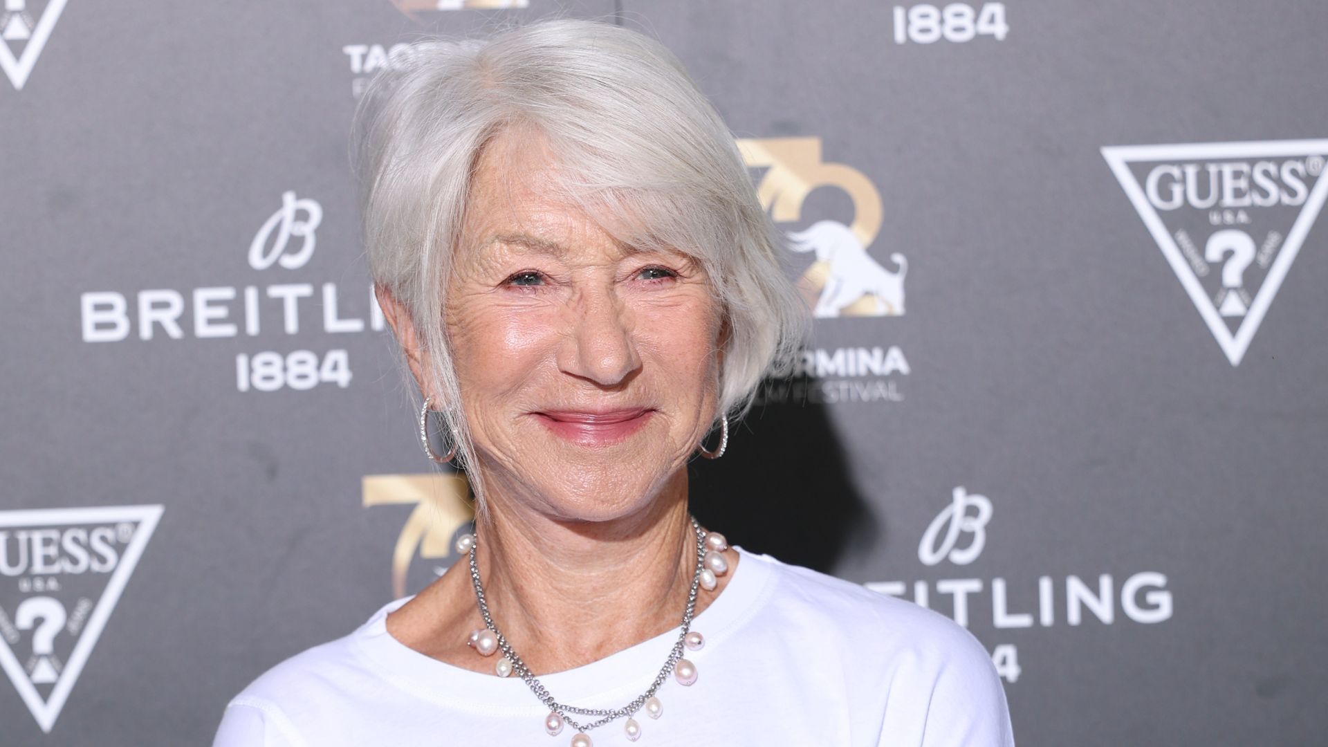 Helen Mirren pictured on the red carpet with short, silver hair, a white T shirt and pearl necklace on