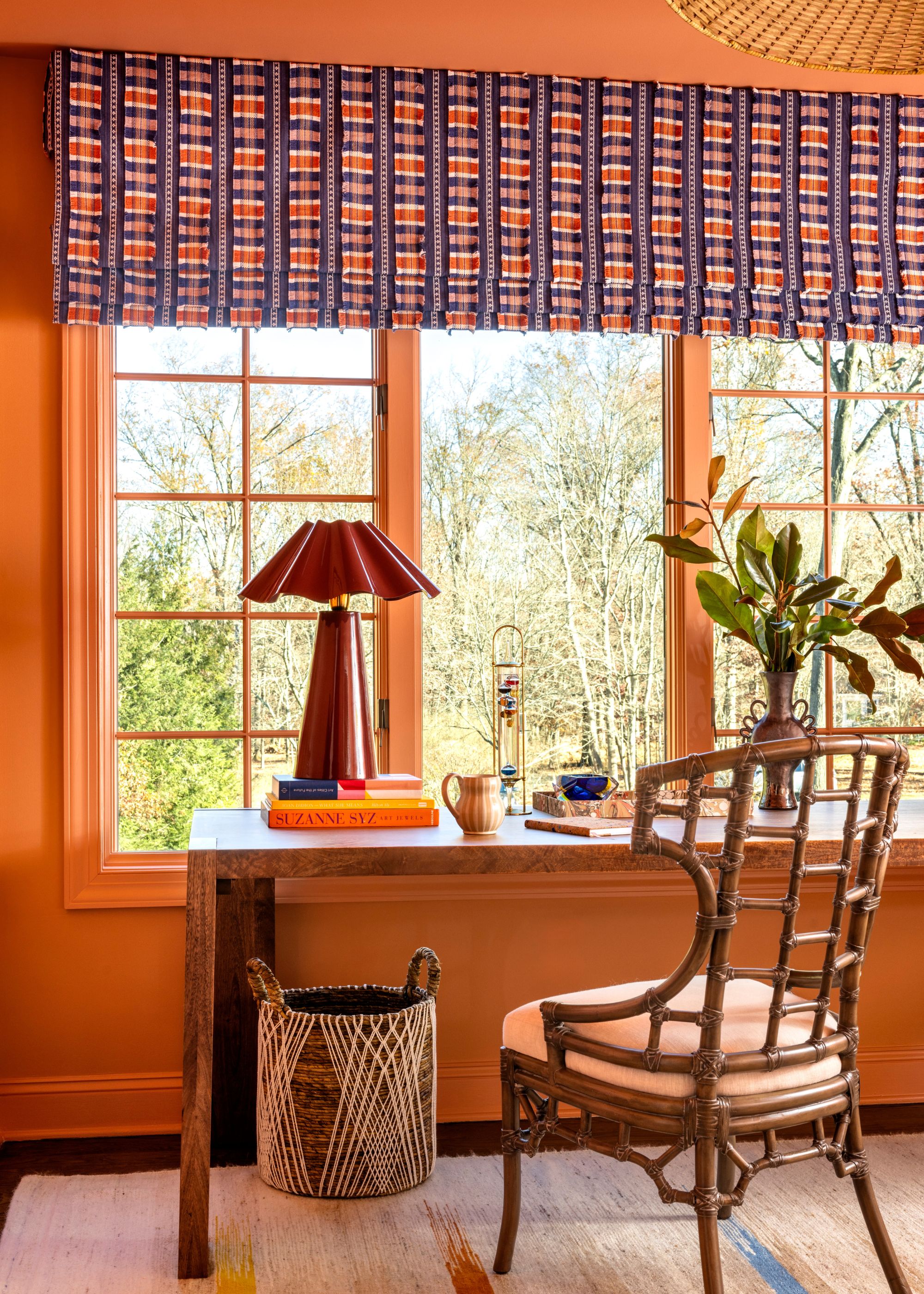 A coral color-drenched home office with a desk in front of a window with a colorful blue and orange blind.