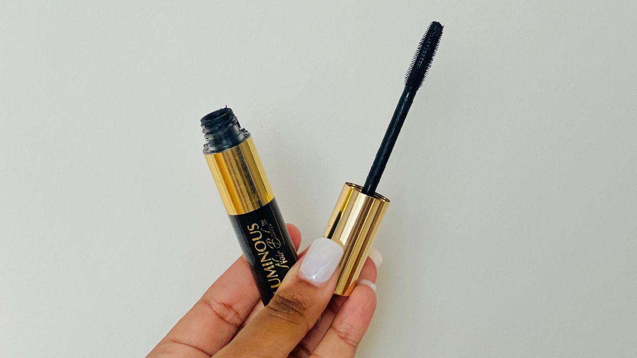 A person holding an opened L'Oreal Voluminous Noir Balm mascara for the best L'oreal mascara.