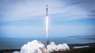 a black and white spacex falcon 9 rocket rocket launches into a blue sky from a seaside pad