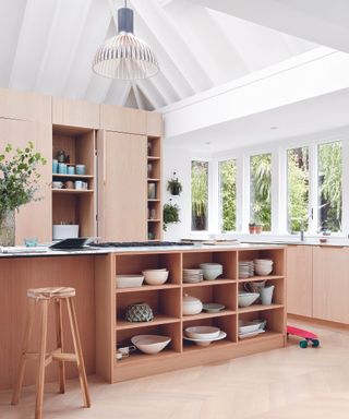 A light and airy kitchen with blush pink cabinets and open shelving storing crockery