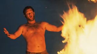 A shirtless Tom Hanks stands in front of a raging camp fire in Cast Away