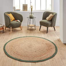 Circular raffia rug with green trim. Two olive green armchairs with yellow pillows and a vase on a green table