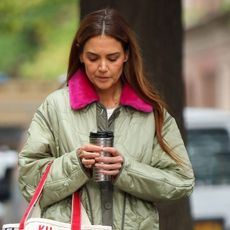 Katie Holmes wears a green jacket and carries a coffee mug