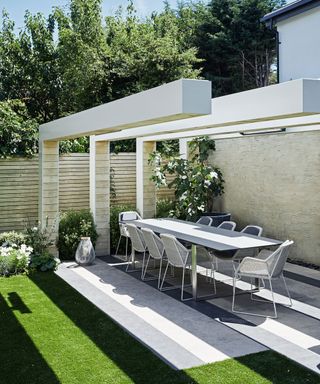 Modern metal patio furniture ideas demonstrated by a long table and chairs underneath a bold architectural feature.