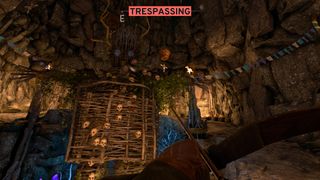 Exploring a cave filled with human skulls and a strange wicker construction in Atomfall with a bow at the ready, the UI informing us we are "trespassing"