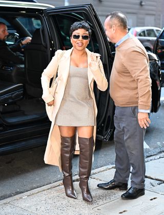 A photo of Quinta Brunson in a brown check mini dress and tall brown boots.