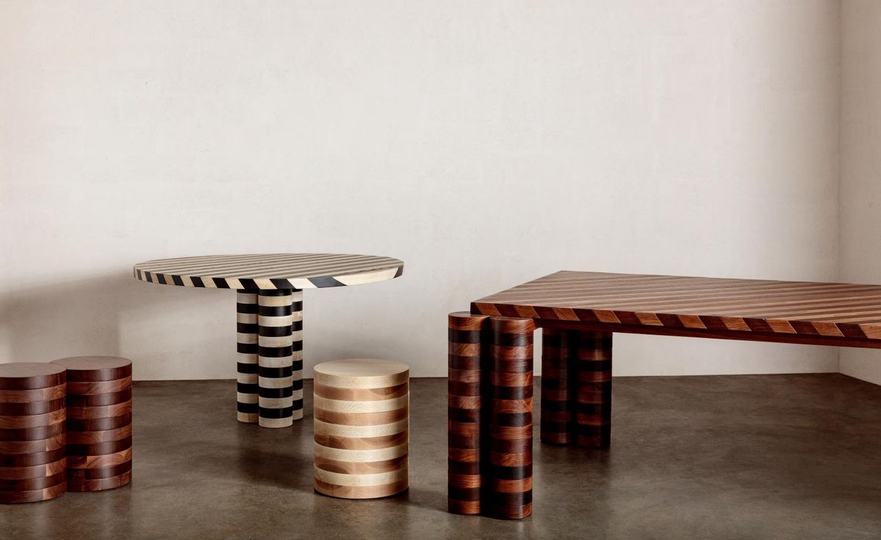 Striped dining and side tables made of angle-cut hardwood photographed in a room with white walled and brown vinyl floor. 