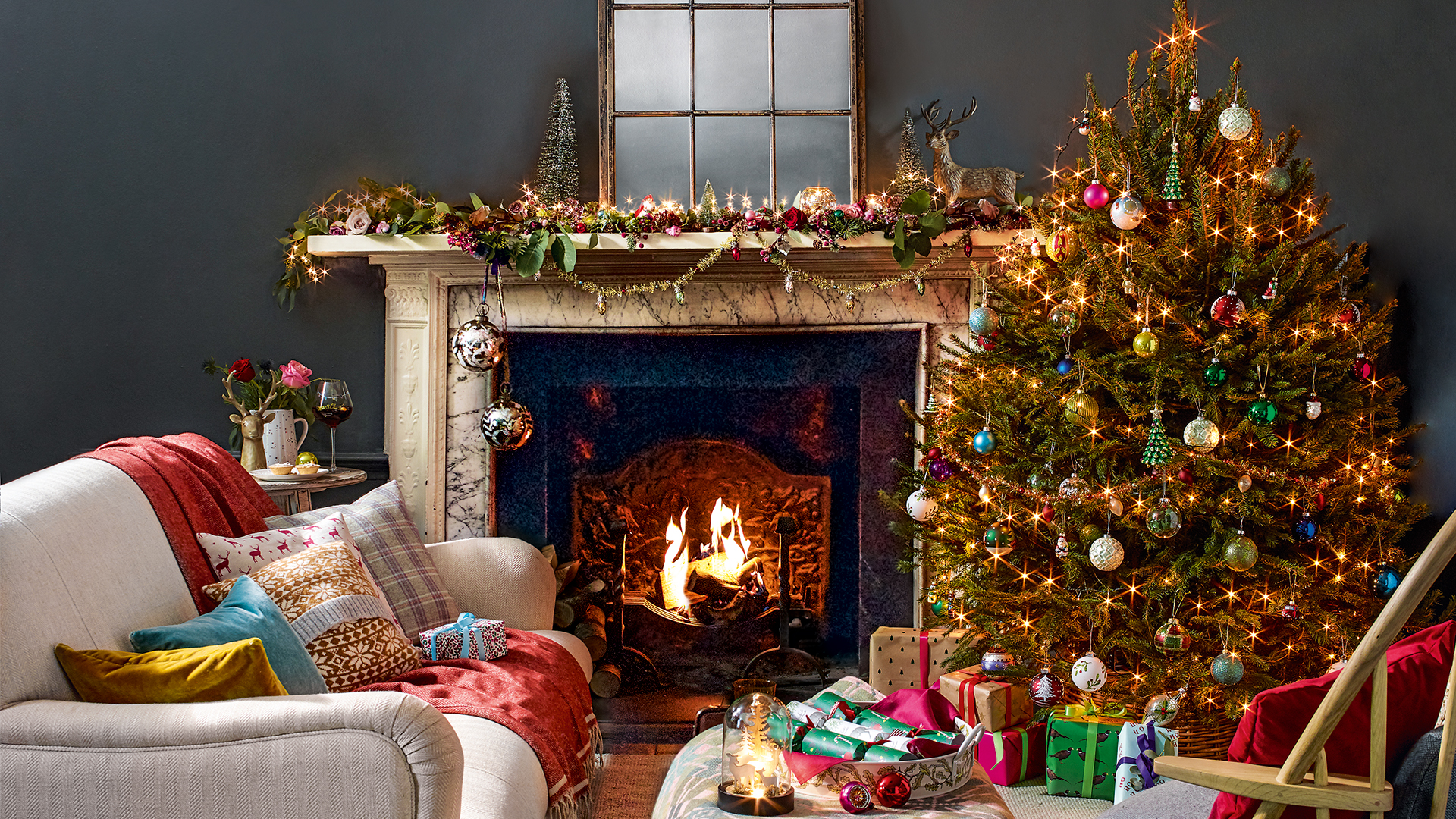 Dark grey living room decorated for Christmas with a style mantlepiece and Christmas tree beside an open fire