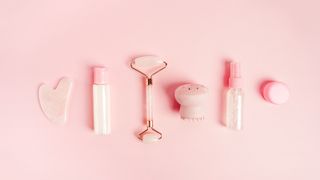 Cosmetics for face care on pink background. Gua sha, lotion, face serum.