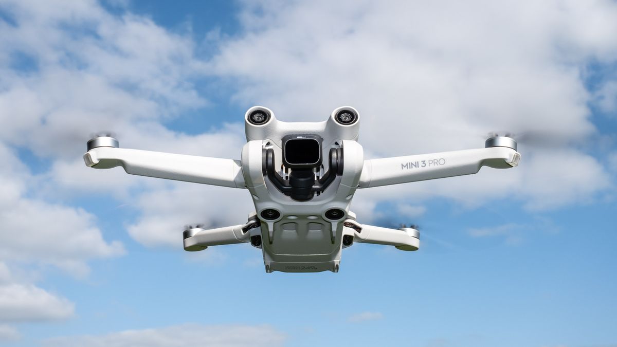 DJI Mini 3 Pro drone in flight with blue sky and clouds background