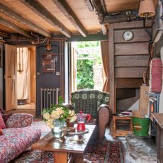 Living room in a rustic cottage with wooden wall panelling, exposed ceiling beams and exposed pipework