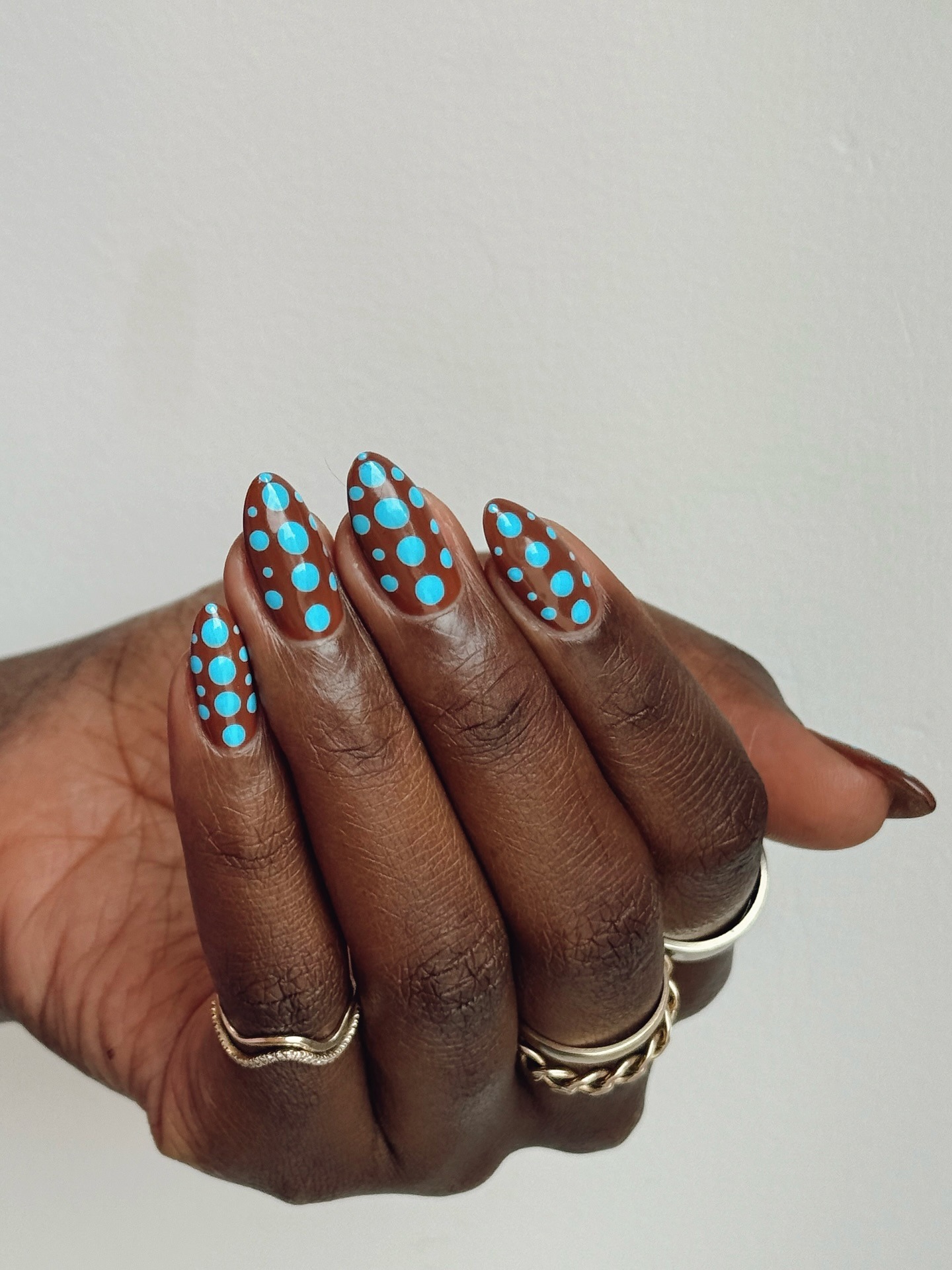 A brown nail design with bright blue polka dots