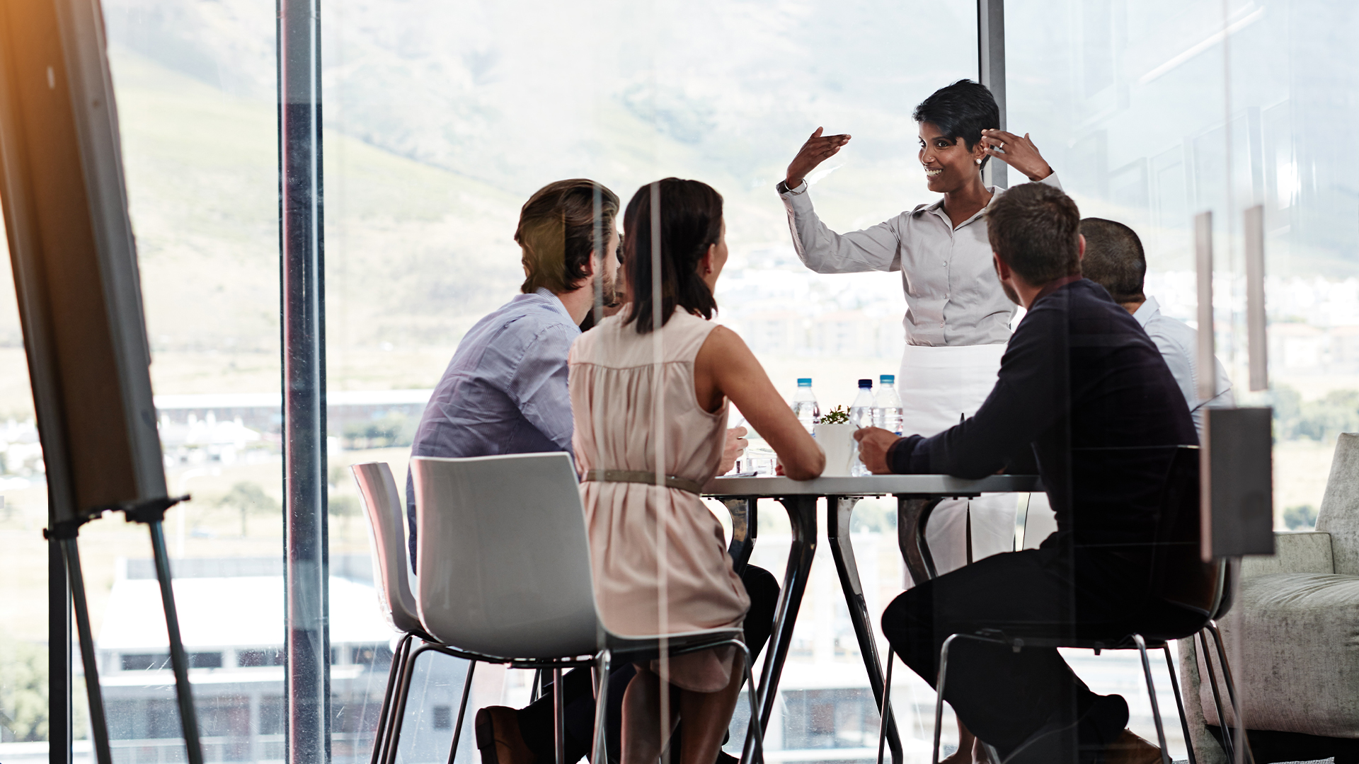 C-suite strategy concept image showing female chief data officer (CDO) standing while talking to colleagues during a boardroom meeting.