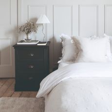 A bedroom with wall panelling and a white-dressed bed