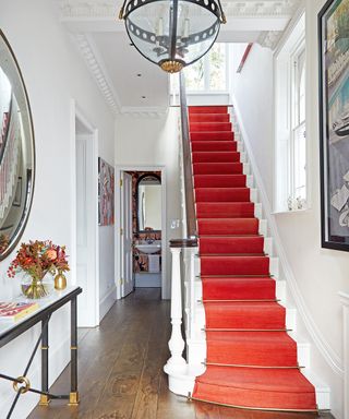 A hallway lighting idea with a red carpeted staircase in a white hall with a Victorian-style ceiling lantern