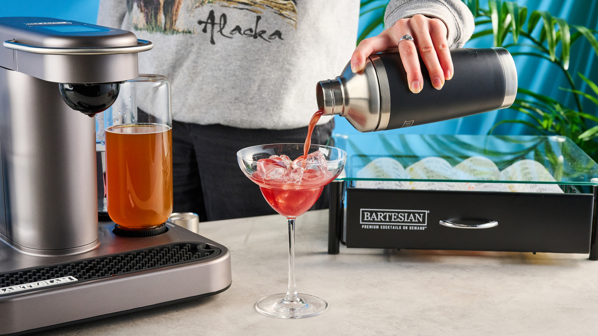 the bartesian premium cocktail machine photographed against a blue background showing its drink-making abilities and accessories and functionality with cocktail pods