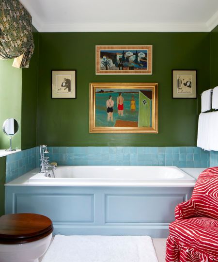 A bathroom with deep green walls, a clue bath surround, and light blue zellige tiles acting as a bath backsplash