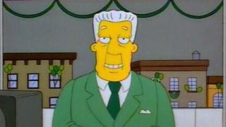 Kent Brockman smiling at the camera and wearing a green suit