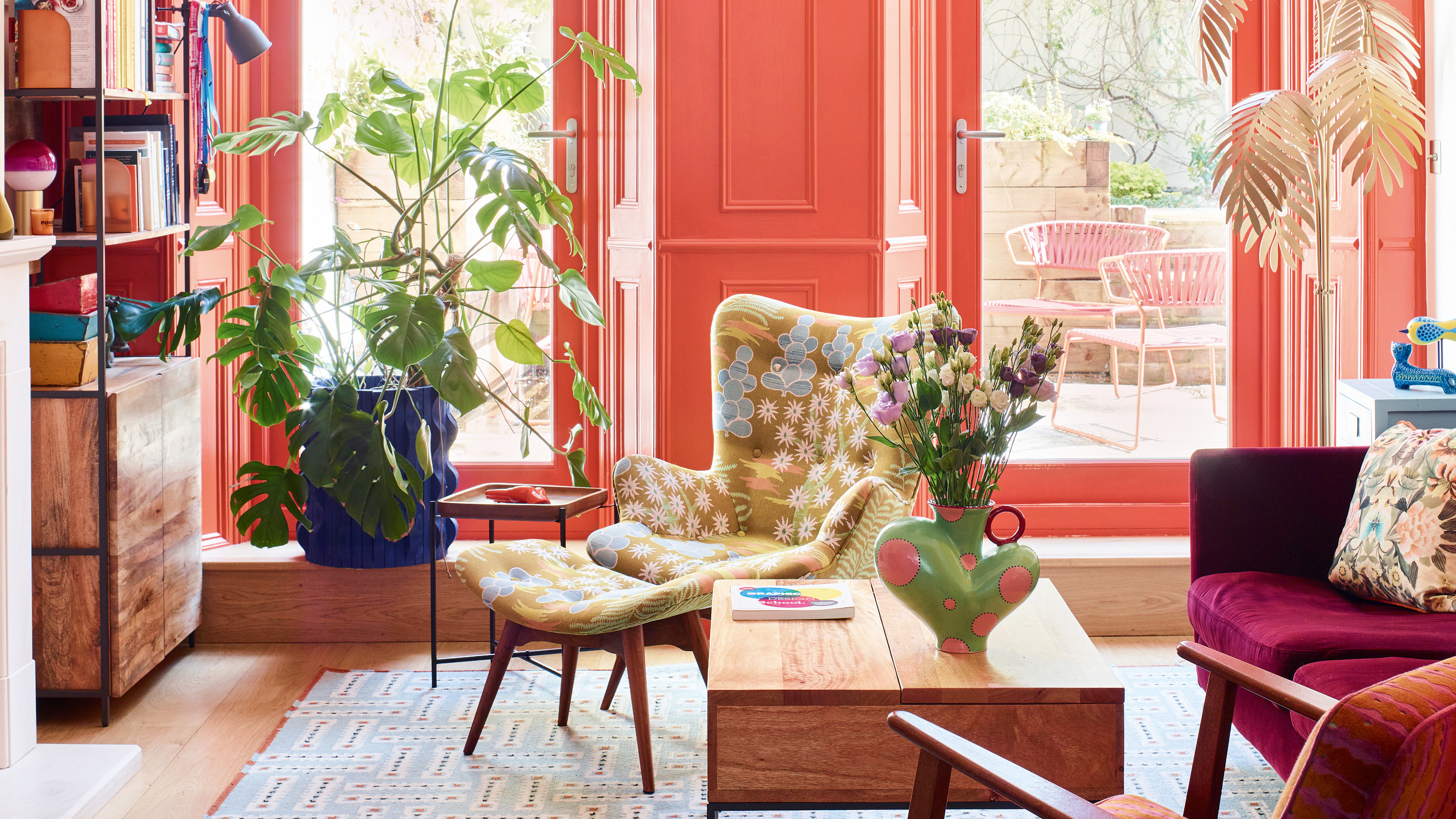 Coral living area with pink, terracotta and lime green seating, industrial wood coffee table and shelving, cobalt blue plant pot and blue and red patterned rug