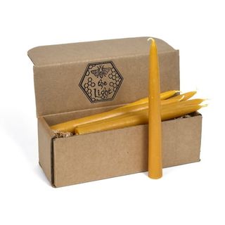 A cardboard box with yellow beeswax candles. One candle standing upright in front of the box. 