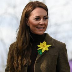 Kate Middleton wearing a tweed jacket and daffodil pin smiling and looking to the right