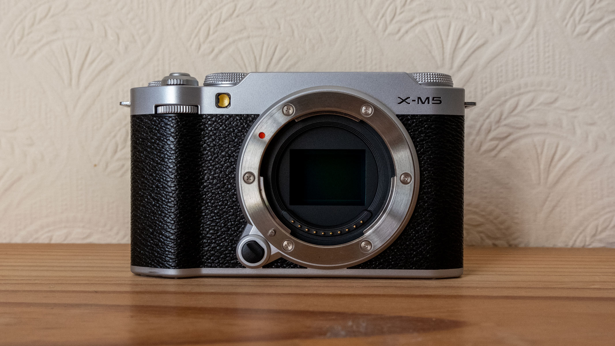 The front of the Fujifilm X-M5 on a wooden shelf.