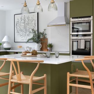 Green kitchen island with white marble top and wooden chairs