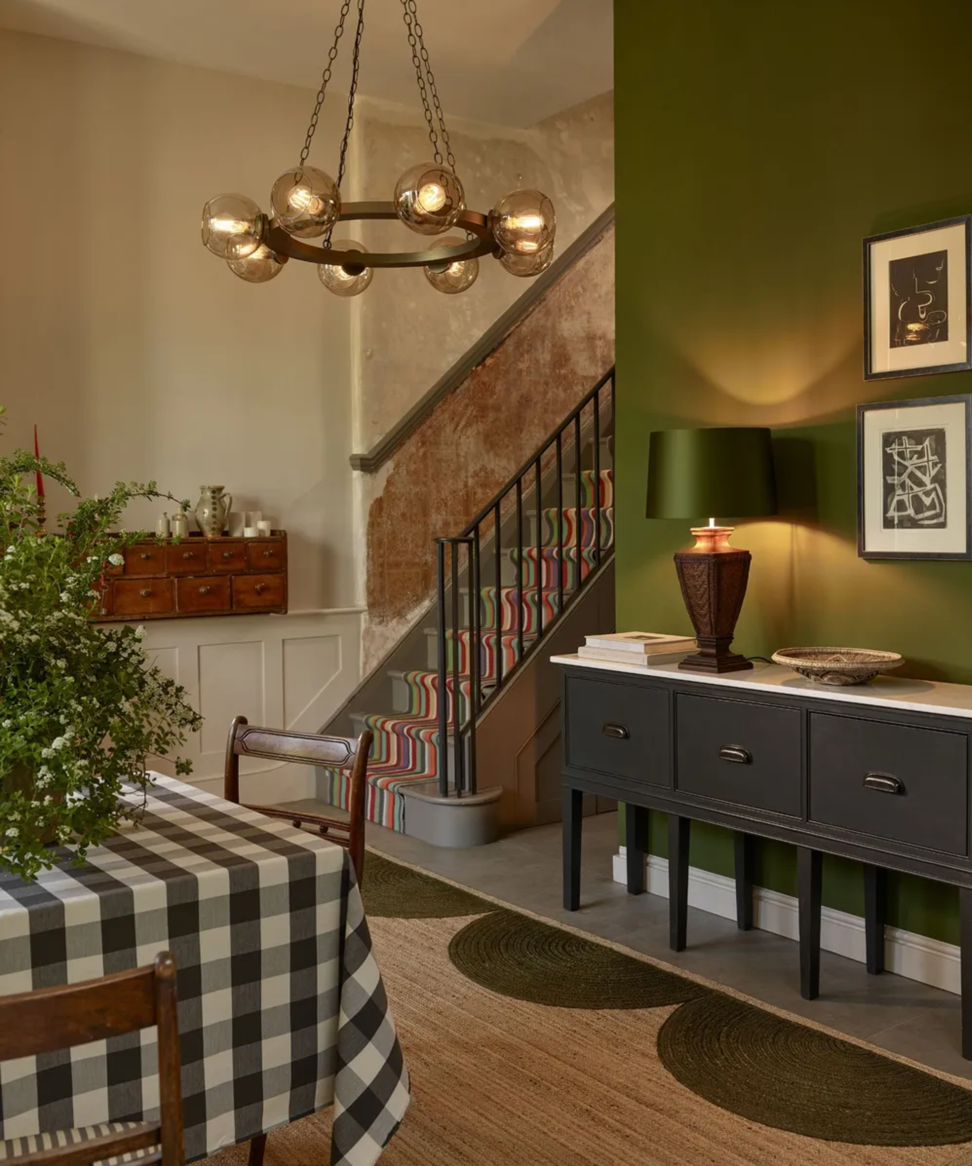 a dining room with a jute rug, a black console table, a lamp turned on, a dining table with a checker printed table cloth, and green painted walls