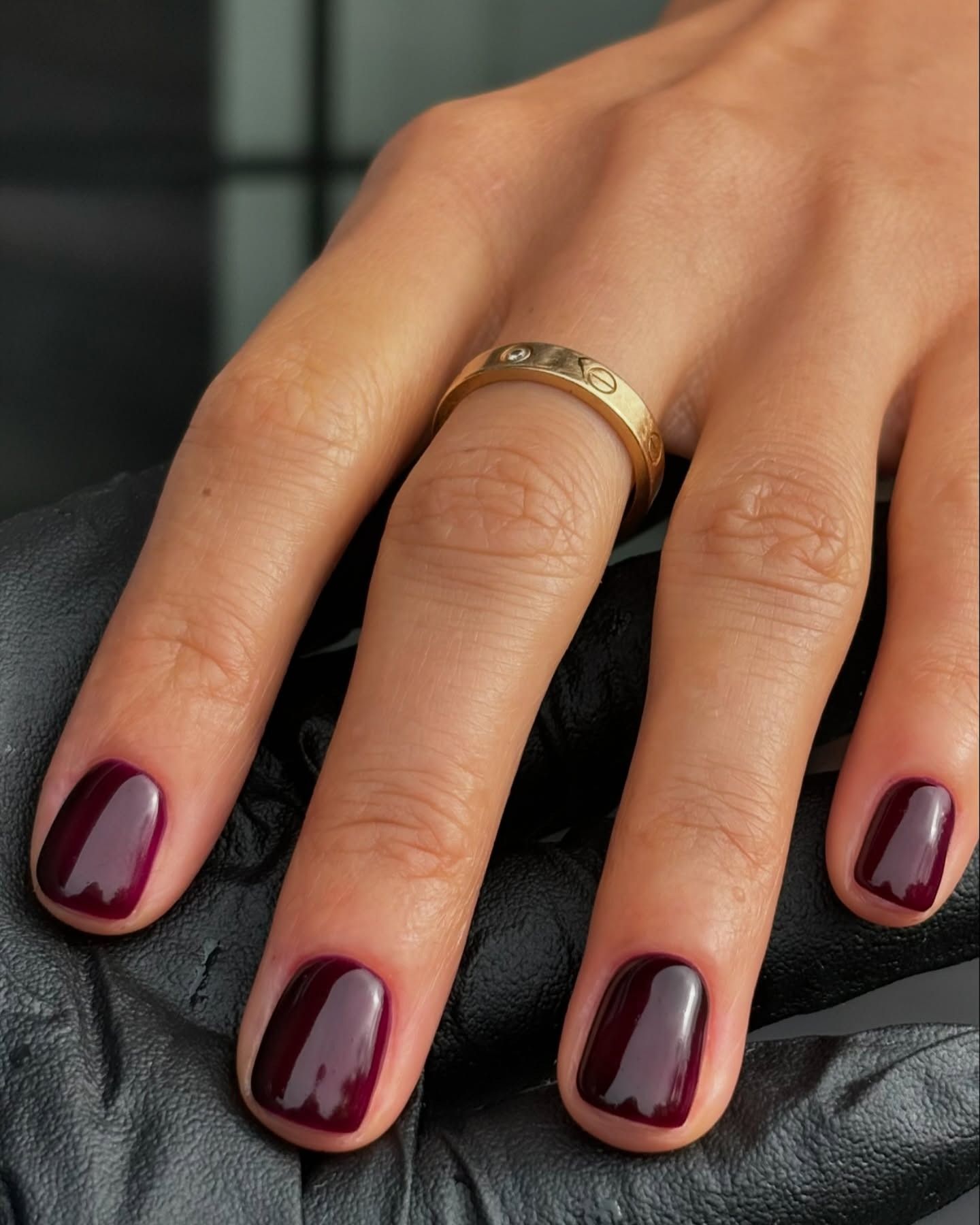 Short dark red nails with a gold cartier ring