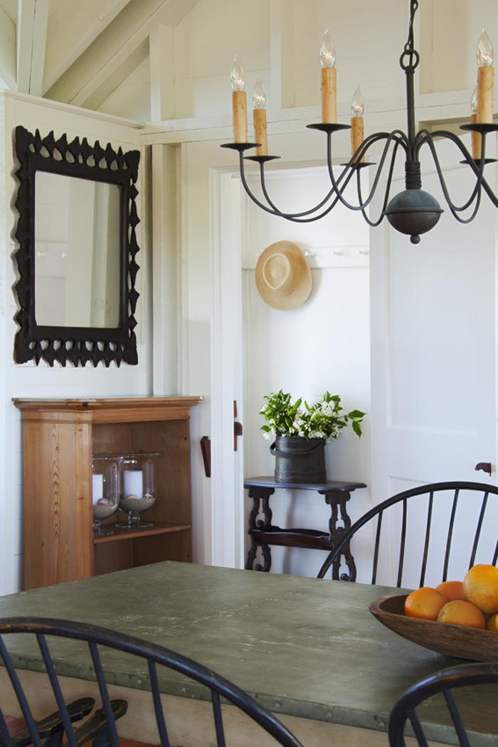A traditionally decorated living room features wooden and wrought iron furniture including a large mirror, a chandelier, and a dining table.