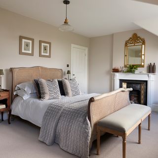 grey painted bedroom with rattan double bed frame, antique mirror and fireplace