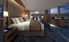 A room in the Shangri-La at the Shard hotel. A large bed sits against the wall and looks over the panoramic view of the city at sunset, through floor-to-ceiling windows that stretch around the entire room.