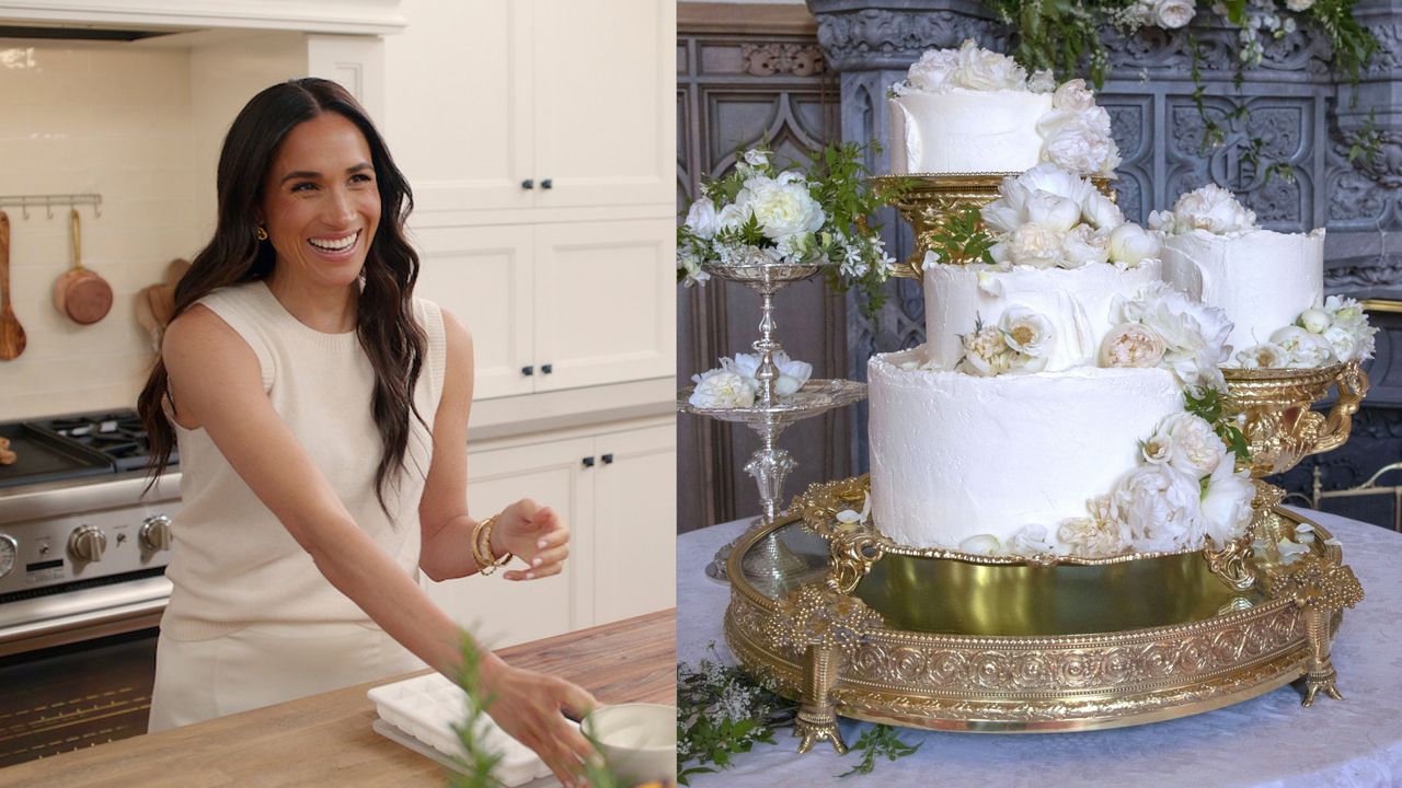 Meghan Markle wearing a beige sleeveless sweater standing in a kitchen laughing next to a photo of her white tiered wedding cake with flowers