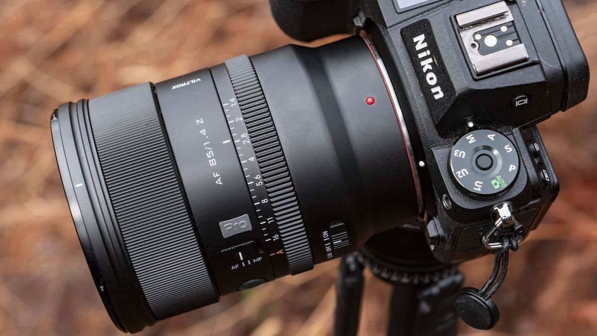 Viltrox AF 85mm F1.4 Pro lens attached to a Nikon camera, mounted to a tripod outdoors and with bronze-colored ferns in the background