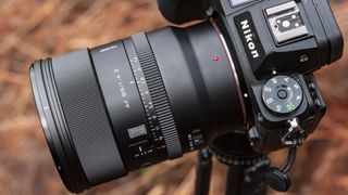 Viltrox AF 85mm F1.4 Pro lens attached to a Nikon camera, mounted to a tripod outdoors and with bronze-colored ferns in the background