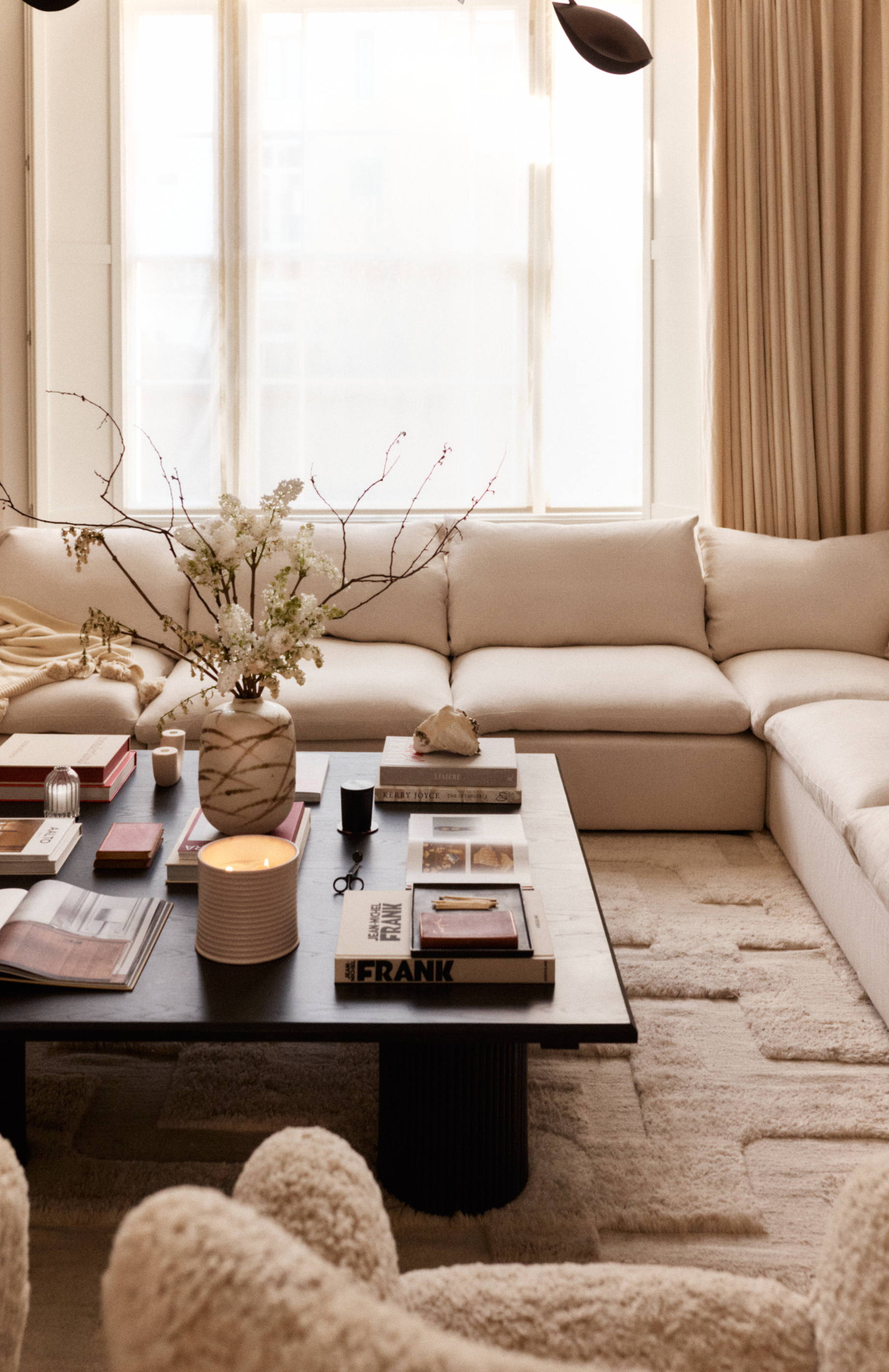 A contemporary living room with a square coffee table, with an assortment of objects arranged on top