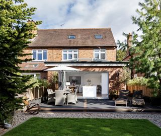 A semi-detached red brick house with a rear extension and garden terrace with patio furniture