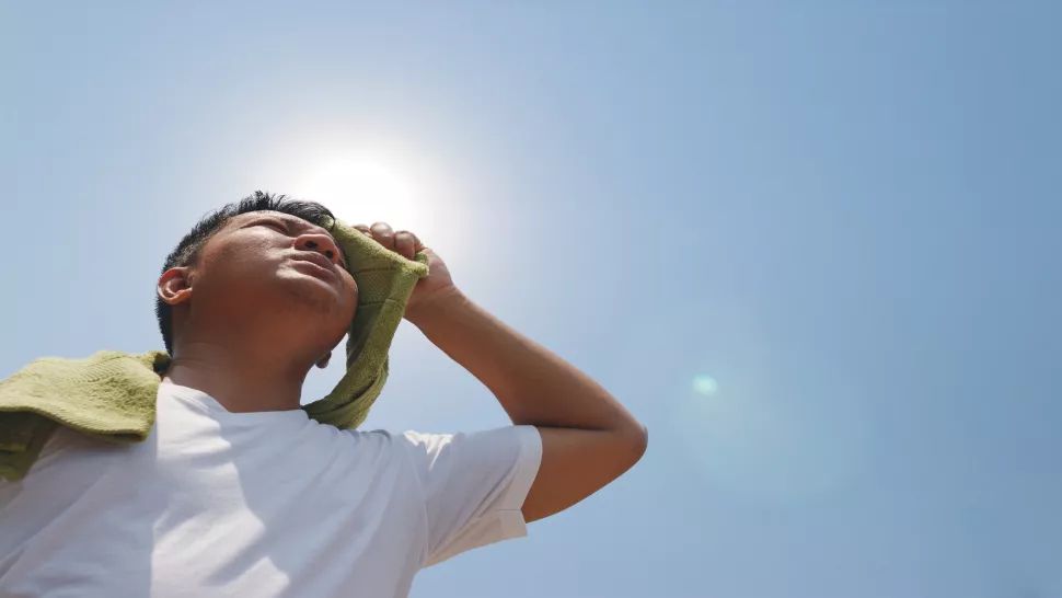 A man wiping sweat from his face under the hot sun.