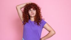 Young woman with curly red hair is scratching her head with a confused expression on her face