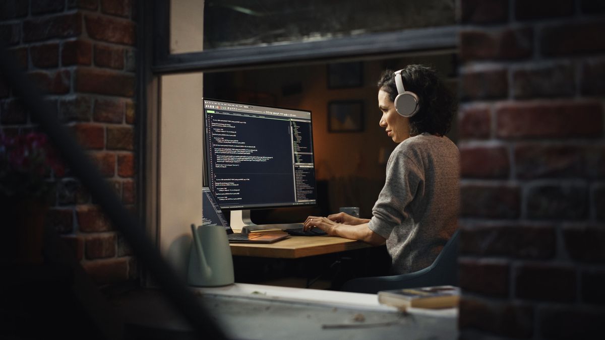 View through window showing female CISO at her desk in a remote work environment with code terminal on monintor