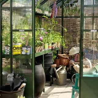 Flowering plants, herb rack and potting bench inside green-framed glass greenhouse