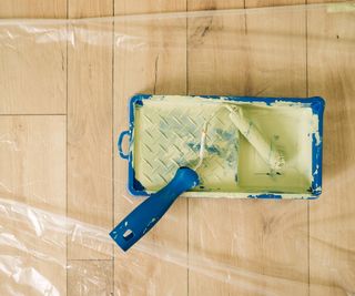 Small paint tray and paint roller on plastic sheeting on wooden floor