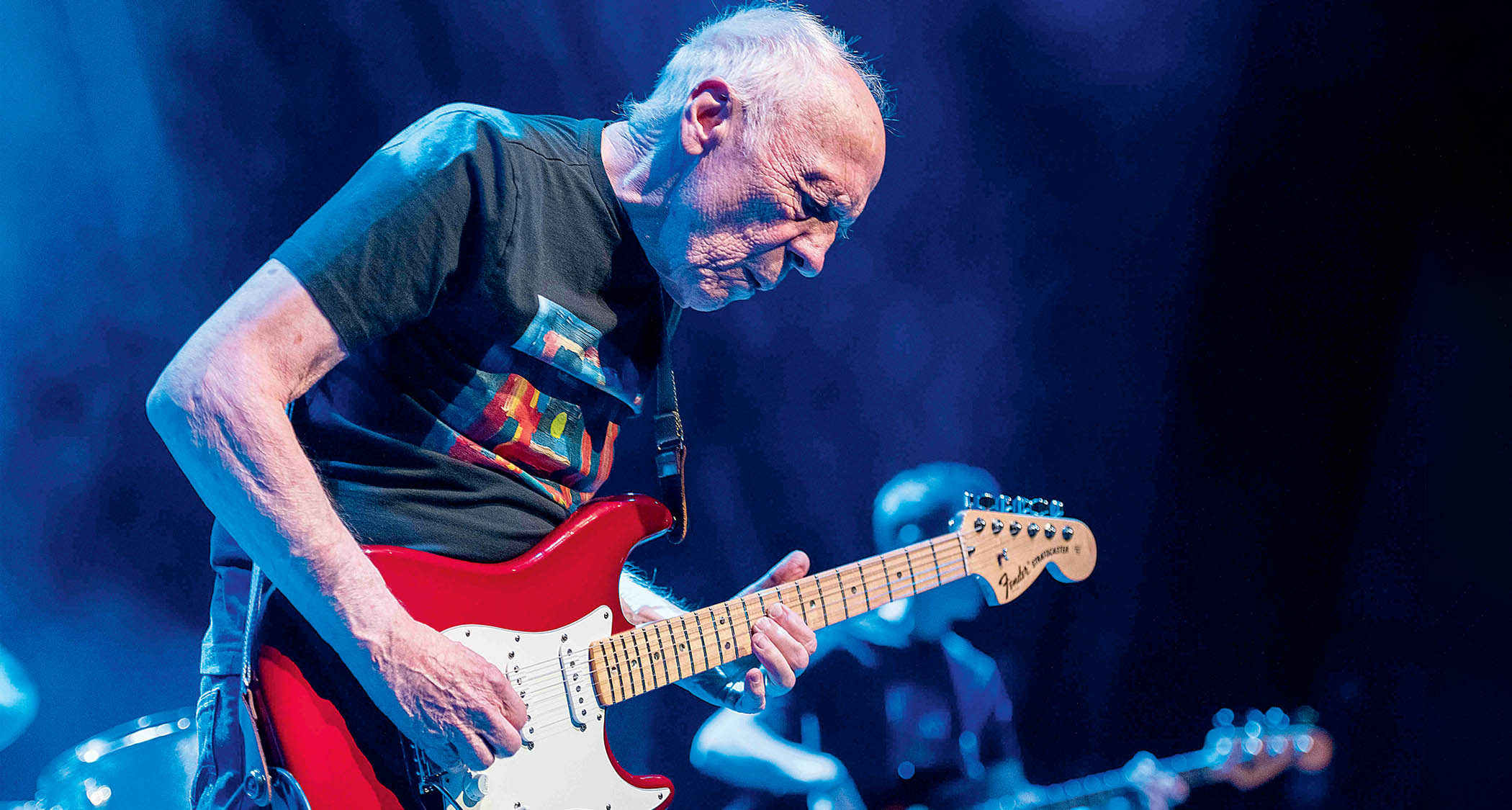 Robin Trower plays his red signature Stratocaster on a stage lit up in blue.