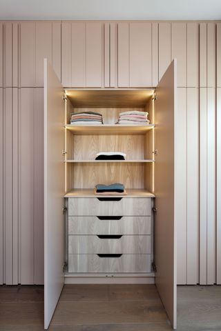 closet doors in pale pink with a section open to reveal drawers and shelving, LED lighting, wooden floor