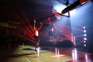 An image shot at a high ISO, cleaned up in-camera with Canon's AI denoise feature on the Canon EOS R5 Mark II. The image shows two basketball players competing on a court illuminated by artistic laser lights